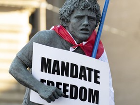 A statue of Terry Fox is decorated with a Canadian flag, protest sign and hat by protesters supporting the 
"Freedom Convoy" to protest vaccine mandates required to cross the US border.