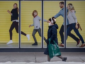 File: A pedestrian wearing a mask walks past a mural of a family enjoying a leisurely maskless walk in Toronto.