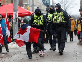 A child wrapped in a Canadian maple leaf flag plays soccer in front of police officers, as truckers and supporters continue to protest in Ottawa on Feb. 9.