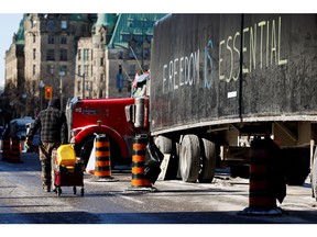 A demonstrator wheels gas cans down the street in front of Parliament Hill and past a slogan painted on the side of a parked truck.