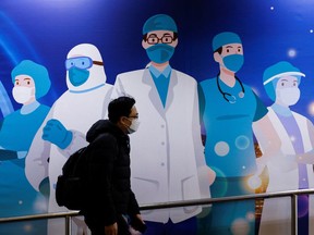 Files: A man wearing a face mask walks past an advertisement to support medical professionals.