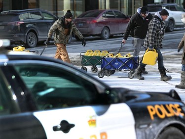 Three men take full cans of fuel past the police on O' Connor Street in Ottawa, Monday morning.