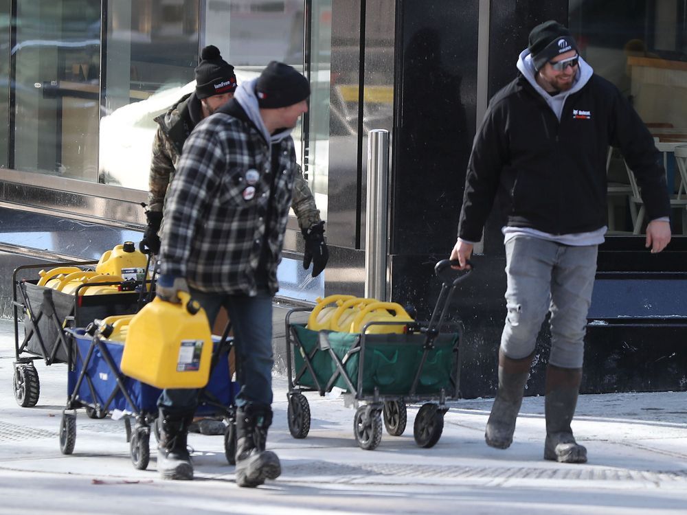 Truckers occupation and protesting continues its 18th day in downtown Ottawa Sunday afternoon. Three men take full cans of fuel past the police on O' Connor Street in Ottawa, Monday morning.