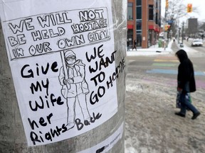 A woman walks past a sign on Bank Street in Ottawa Friday. The sign said "We will not be held hostage in our city."