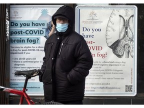 TORONTO, ONTARIO: JANUARY 4, 2022--PANDEMIC-A pedestrian wearing a mask walks past posters asking "Do you have post-Covid brain fog?" on Toronto's Danforth Avenue in Toronto during the Covid 19 pandemic, Tuesday January 4, 2022. 

[Peter J Thompson]  [National Post story by TBA/National Post]