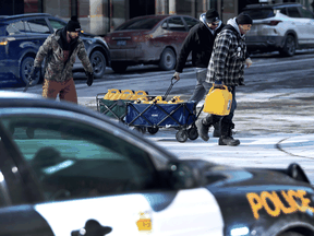 Three men take full cans of fuel past the police in Ottawa on Monday.