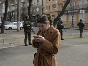 A woman looks at her cellphone as soldiers stand guard outside a government building hit by Russian rockets on March 29 in Mykolaiv, Ukraine.