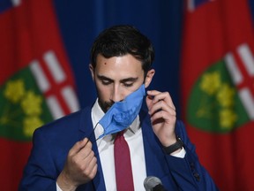 Ontario Education Minister Stephen Lecce takes his mask off before answering questions at a press conference. Soon many people won't be wearing masks at all.