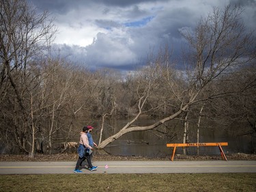 People walk by a barrier that had been recently placed between the Rideau River's edge and the nearby paved pathway.