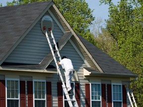 A person climbing an extension ladder on a two-storey suburban home.