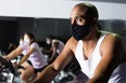 Man in protective mask ride stationary bike in fitness club