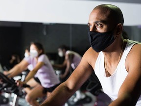 Man in protective mask ride stationary bike in fitness club