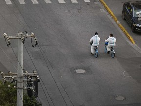Workers wearing personal protective equipment (PPE) ride bicycles on a street during a COVID-19 lockdown in the Jing'an district in Shanghai on April 9, 2022.