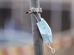 A rebellious disposable face mask is hanging from a street sign pole.