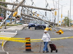 A woman walks around barricades on Merivale Road with downed power lines caused by last weekend's storm. Tuesday, May. 24, 2022.