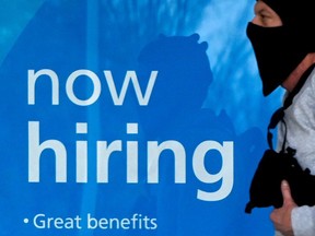 A man walks past a "now hiring" sign in front of a store.