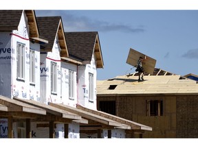 A builder carries a sheet of wood on the roof of a home in a new Ottawa subdivision.