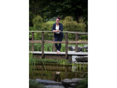 Tina Boileau stands on a bridge overlooking a pond in the gardens of the cemetery.