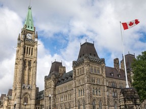 A Panoramic Shot Of Canadian Parliament Building In Ottawa Canada With Blue Skies And Clouds Behind And Canadian Flag Blowing In The Wind