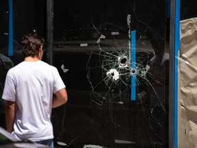 A pedestrian walks past bullet holes in the window of a store front on South Street in Philadelphia, Pennsylvania, the day after a mass shooting left three dead and multiple people injured.