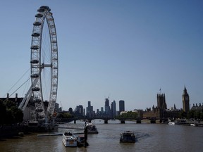 A photograph taken on July 18, 2022 shows the London Eye (L) and the Houses of Parliament (R) next to the River Thames in central London, as the country experiences an extreme heat wave. - Britain could hit 40 C for the first time, forecasters said, causing havoc in a country unprepared for the onslaught of extreme heat that authorities said was putting lives at risk.