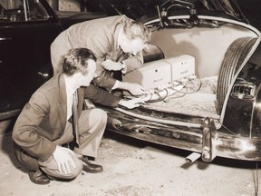 Former owner of Amey's taxi, Francis Greenwood, kneeling, inspects as the first two-way radio is installed in a taxi in Kingston.