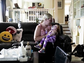 Amanda Jollymore cradles her 2-year-old daughter Mia, who has an unknown genetic syndrome along with other diagnosed medical issues, as they sit on the couch at their home in Ottawa, Monday, June 27, 2022.