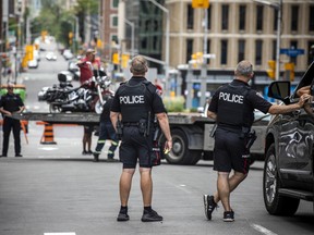 Police officers observe as a tow truck operator removes a motorcycle from the "motor vehicle control zone" in downtown Ottawa Saturday afternoon.