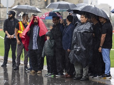 People listen to speakers in a heavy downpour on Parliament Hill during a commemoration of the martyrdom of Imam Hussain, grandson of the Islamic prophet Mohammad, on Monday, Aug. 8, 2022.