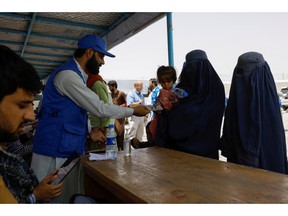 A displaced Afghan woman receives cash aid from a WSTA employee at a distribution centre for displaced people in Kabul, July 28, 2022. About 85 per cent of NGOs have had to close their doors since the Taliban seized power.