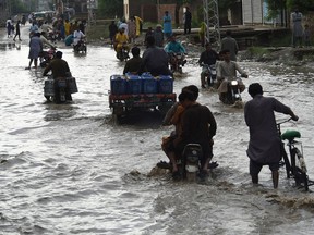 Commuters make their way through a flooded street after heavy monsoon rains in Jacobabad, Sindh province, on August 26, 2022