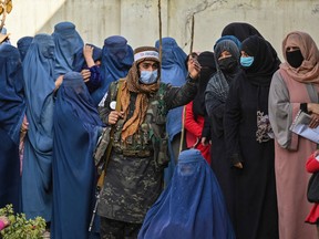 In this file photo taken on Nov. 29, 2021, a Taliban fighter (C) stands guard as women wait during a World Food Programme distribution in Kabul.