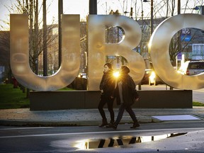 A UBC sign at the campuss main entrance glows in the late evening light while students walk in around the campus.