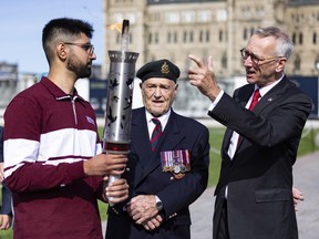 The Canadian Remembrance Torch being lit, for the first time, from the Centennial Flame in Ottawa. It was designed and built by three engineering students from McMaster University. Holding the torch is McMaster student Yuvraj Sandhu with veteran John Preece and Jaap Jan Speelman of the Embassy of the Kingdom of the Netherlands to Canada.