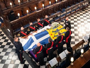 Queen Elizabeth II, top left, and other members of the royal family (not in view) watch as pallbearers arrive with Prince Philip's coffin into the quire of St. George's Chapel for his funeral service, in Windsor Castle on April 17, 2021.