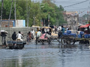 People make their way through flooded street after heavy monsoon rains in Jacobabad, Sindh province, on September 6, 2022. - More than 33 million people in Pakistan have been affected by the flooding, brought on by record monsoon rains that have swamped a third of the country, causing at least 1,300 deaths.