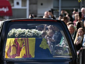 TOPSHOT - Members of the public pay their respects as they hearse carrying the coffin of Queen Elizabeth II, draped in the Royal Standard of Scotland, is driven through Ballater, on September 11, 2022. - Queen Elizabeth II's coffin will travel by road through Scottish towns and villages on Sunday as it begins its final journey from her beloved Scottish retreat of Balmoral. The Queen, who died on September 8, will be taken to the Palace of Holyroodhouse before lying at rest in St Giles' Cathedral, before travelling onwards to London for her funeral.