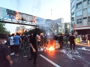TOPSHOT - A picture obtained by AFP outside Iran on September 21, 2022, shows Iranian demonstrators burning a rubbish bin in the capital Tehran during a protest for Mahsa Amini, days after she died in police custody.