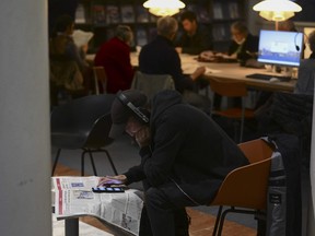 A man reads a newspaper and uses his smart phone at a public library.