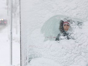 A woman waits for a bus on Smyth Road after an overnight snow storm in Ottawa Friday.