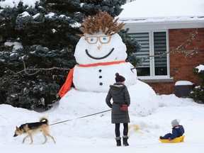 Liz Fee, her daughter Quinn and their dog Nanook walk past a giant snowman on Browning Ave in Ottawa Monday.