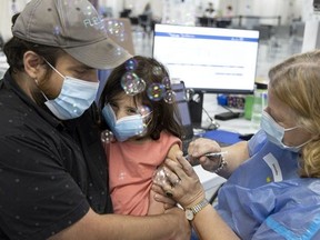 Vincent Garneau holds his four-year-old daughter, Simone, as she gets her first shot of the COVID-19 vaccine at the Décaire Square vaccination centre in Montreal on Monday, July 25, 2022. A health-care worker blows bubbles and plays with Simone as she receives the vaccination.