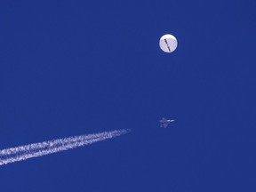 In this photo provided by Chad Fish, a large balloon drifts above the Atlantic Ocean, just off the coast of South Carolina, with a fighter jet and its contrail seen below it, Saturday, Feb. 4, 2023. The balloon was struck by a missile from an F-22 fighter just off Myrtle Beach, fascinating sky-watchers across a populous area known as the Grand Strand for its miles of beaches that draw retirees and vacationers.