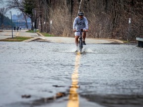 File photo: Cyclists peddled through the Ottawa River that was flowing over the east end of Rue Jacques-Cartier in Gatineau, Saturday, April 22, 2023. As of early Monday evening, sections of the Ottawa River Pathway were closed by the National Capital Commission due to flooding.