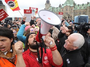 Public Service Alliance of Canada National President Chris Aylward (in the black coat) and PSAC's Regional Executive Vice-President for the National Capital Region Alex Silas (in the red jacket) speak to the media and striking federal workers on Parliament Hill April 26, 2023.