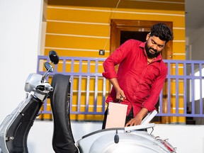 A young man in India takes the battery out from an electric scooter.