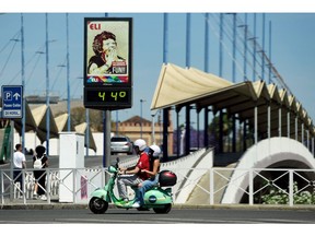 TOPSHOT - A couple ride a Vespa motorcycle past a street thermometer reading 44 degrees Celsius in Seville on April 26, 2023 as Spain is bracing for an early heat wave. - Spain, which in 2022 experienced the hottest year since records began, is bracing for an early heat wave later this week that will cause temperatures to soar to levels normally seen in summer. State weather office AEMET forecasts the mercury could hit 40 degrees Celsius (104 degrees Fahrenheit) in the southern Guadalquivir Valley. (Photo by CRISTINA QUICLER / AFP)