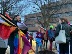 Clayton Goodwin, left, holds rainbow flags as people meet in the parking lot outside the Ottawa-Carleton District School Board headquarters building before a board meeting on Tuesday evening.