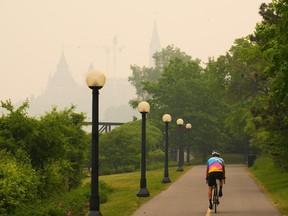 A cyclist rides as smoke from wildfires in Ontario and Quebec obscures Parliament Hill in Ottawa on Tuesday, June 6, 2023.