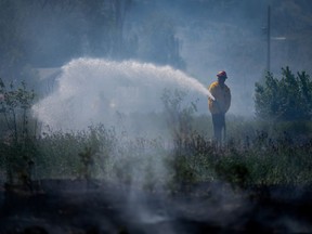 A firefighter directs water on a grass fire on an acreage behind a residential property in Kamloops, B.C., Monday, June 5, 2023.